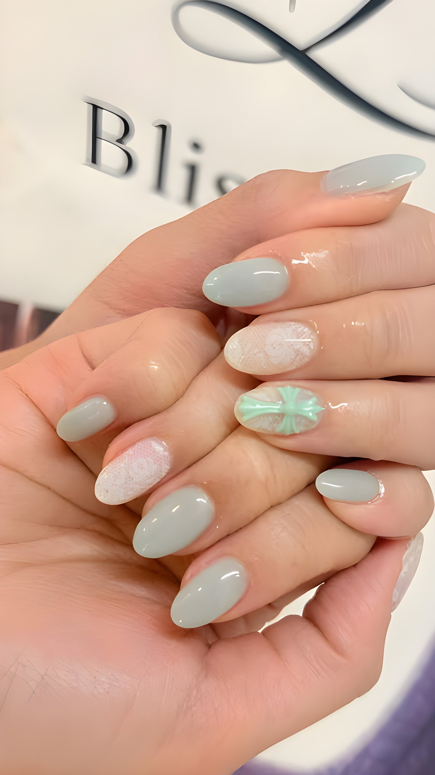 Sage gel almond nails with white lace art and a mint cross charm